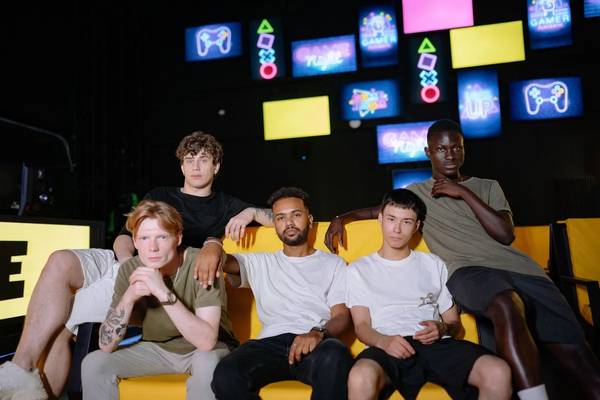 Five friends sitting together on a yellow couch in a gaming lounge, under a wall of neon arcade signs