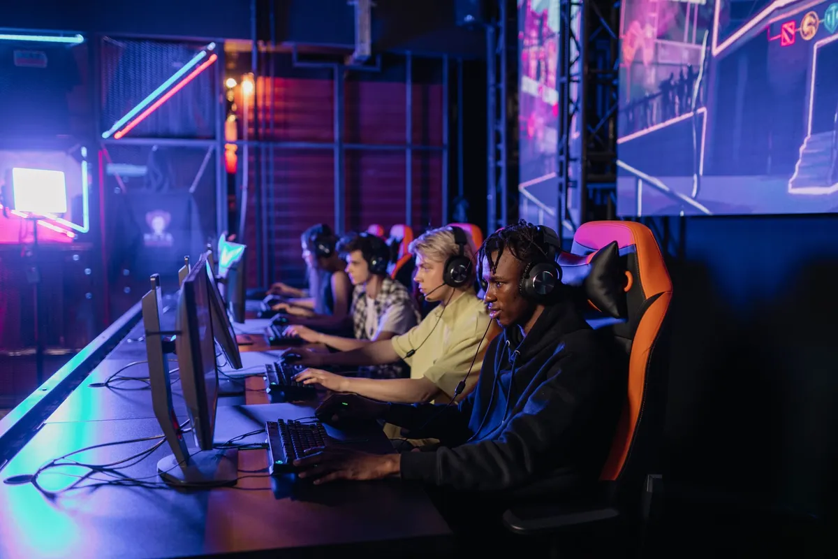 A row of players in headsets competing at PCs along a lit esports arena desk