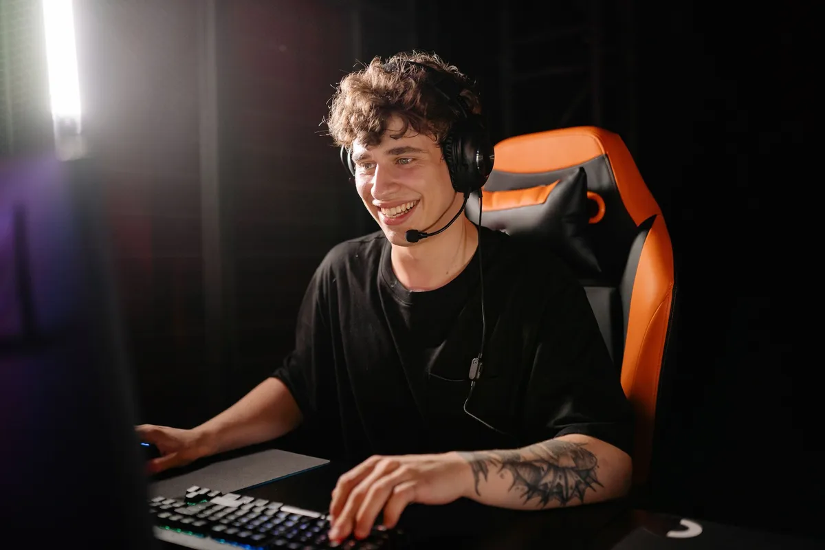 A streamer in a headset smiling at his monitor with his hands on a lit keyboard