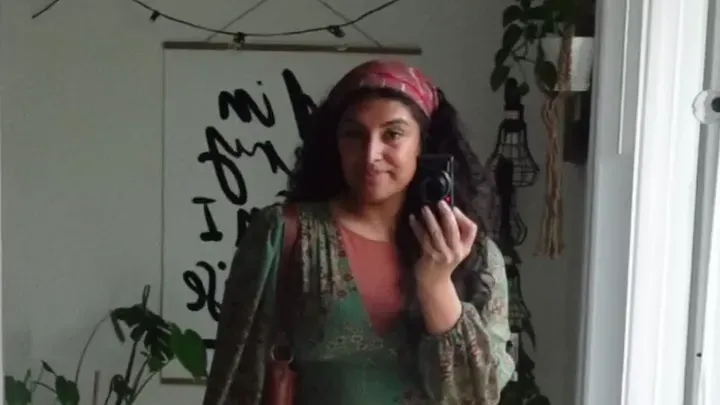 Creator in a green dress and headscarf filming herself in a mirror