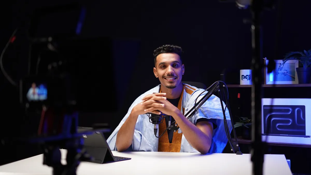 A creator seated at a studio desk behind a microphone, filmed by a camera on a tripod
