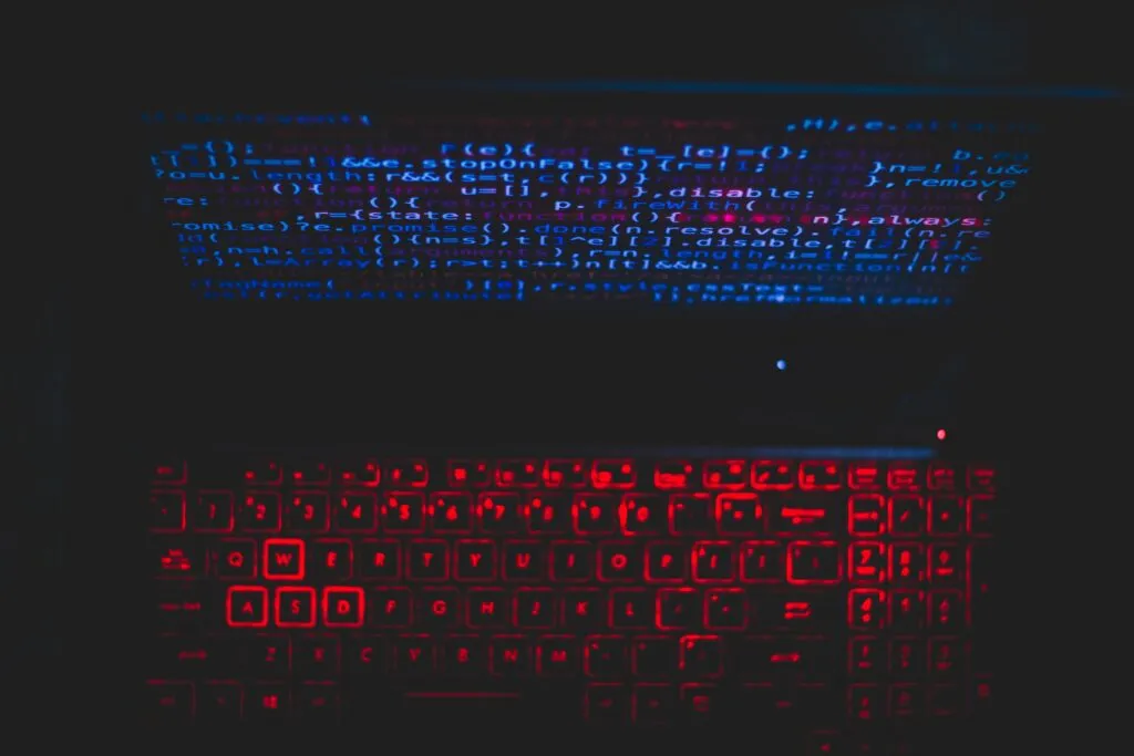 Dark laptop with red backlit keyboard and blue lines of code on the screen