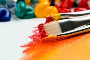 Two paintbrushes loaded with red and orange acrylic paint on white paper