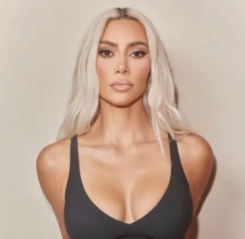 Kim Kardashian with platinum blonde hair in a black tank top against a neutral backdrop