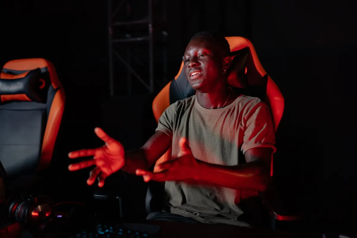 A creator in a gaming chair gesturing mid-sentence to camera under red studio light