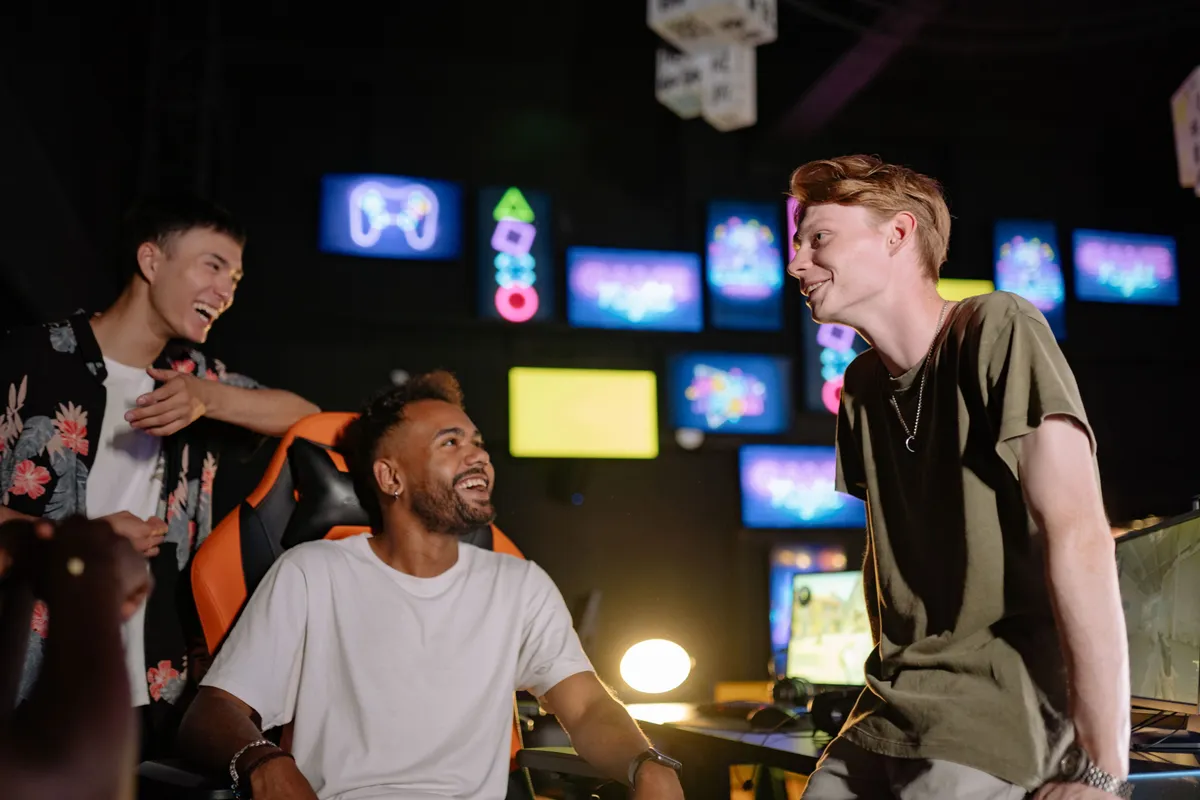 Three friends laughing together in a neon-lit arcade full of screens