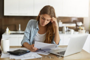 Young woman doing taxes, looking at paperwork with laptop and calculator