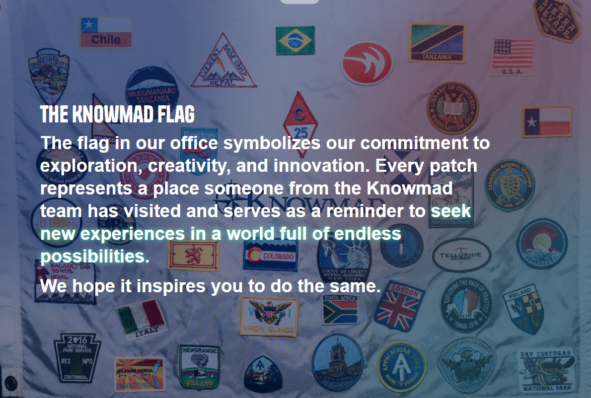A high-angle, close-up shot shows "The Knowmad Flag," a light-colored fabric banner covered in a dense, colorful collage of travel patches and national flags. The patches represent various global destinations, including Chile, Brazil, Tanzania, Nepal’s Everest Base Camp, and several U.S. states like Texas and Colorado. Overlaid in the center is white and teal text explaining that the flag symbolizes the team’s commitment to exploration and innovation, with each patch marking a location visited by a team member. The background is slightly dimmed to make the inspirational message about seeking new experiences stand out clearly against the vibrant, embroidered textures of the patches.